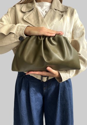 Borsa a tracolla in pelle verde oliva con parte superiore arricciata, texture liscia e base rettangolare, tenuta con entrambe le mani davanti a uno sfondo neutro.