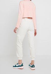 Vita cargo-joggers med elastiska fållar och fickor, tillsammans med en ljusrosa croppad tröja och sportiga sneakers med turkosa detaljer.