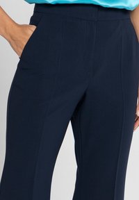 Granatowe spodnie o dopasowanym kroju, wykonane z gładkiego materiału, z bocznymi kieszeniami i prostą nogawką, wzbogacone subtelnymi detalami w postaci fałdki z przodu.