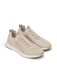 Sneakers in maglia beige con lacci elastici e linguette di sollevamento. Presentano un tessuto testurizzato sulla parte superiore e una suola bianca liscia con un accento in gomma marrone chiaro.