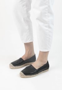 Zwarte leren espadrilles met een jute touwzool, voorzien van een ronde neus en gestikte accenten. Geraadpleegd met witte cropped broeken.