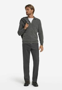 Grauer Reißverschluss-Kardigan aus weichem Strickmaterial, kombiniert mit dunkeltgrauen Hosen und schwarzen Schuhen. Mit Kragen und Taschen-Details.