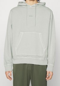 Ljust grön sweatshirt med huva, framficka och ribbad muddar. Har en diskret "BOSS"-logotyp i mitten. Mjuk tygtextur.