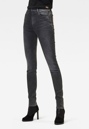 Jeans skinny en denim gris foncé avec une finition délavée, présentant un design classique à cinq poches et de subtils détails de couture le long des côtés.