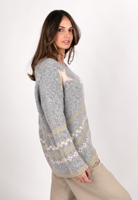 Grauer gestrickter Pullover mit lockerer Passform, der ein Sternenmuster in Creme, metallischen goldenen Streifen und einer strukturierten Oberfläche aufweist.