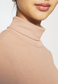 Ljusrosa ribbade polotröja med en figurnära passform och hög krage. Slät textur, sömsynliga detaljer vid axeln.