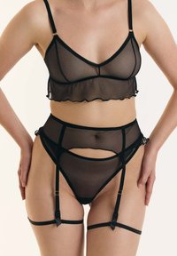 Zwart lingeriesetje met transparante mesh bralette met franje, hoge taille slip met uitsparingen en verstelbare kousenbanden. Minimalistisch ontwerp.
