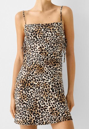 Leopardenmusterkleid mit verstellbaren Trägern, quadratischem Ausschnitt und seitlichen Bindebändern. Hergestellt aus glattem Stoff, mit schwarzen und braunen Punkten auf einem beigen Hintergrund.