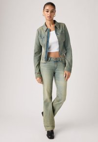 Τζιν μπουφάν και παντελόνι καμπάνα σε ανοιχτό γαλάζιο-πράσινο. Το μπουφάν έχει δύο μπροστινές τσέπες και κοντή γραμμή· το παντελόνι διαθέτει θηλιές για ζώνη και κλασική εφαρμογή.