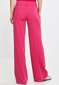 Różowe spodnie o szerokich nogawkach o gładkiej teksturze, wykonane z lekkiego materiału, z tylnymi kieszeniami i prostymi nogawkami.