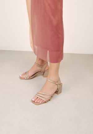 Riemchen-Sandalen mit Blockabsatz in metallischem Champagnerfarbton. Verfügt über eine schimmernde Textur und einen Knöchelriemen mit einem kleinen Schnallen-Detail.