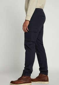 Marine cargobroek met elastische cuffs, meerdere zijzakken en een knoopzak achter. Materiaal lijkt duurzaam met een gladde textuur.