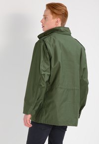 Jachetă verde, de lungime medie, confecționată dintr-o țesătură ușoară. Dispune de un guler înalt, buzunare laterale și o talie ușor strânsă. Design simplu.