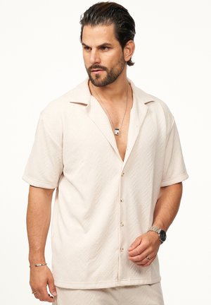 Short-sleeve, light beige shirt in textured fabric. Features a notched collar, button front, and geometric pattern throughout.