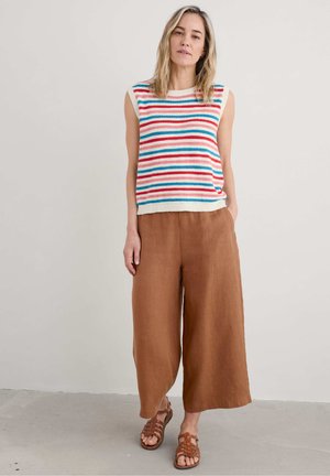Top senza maniche a maglia a righe in crema, blu e rosso; abbinato a pantaloni in lino a gamba larga marroni e sandali marroni con cinturini.