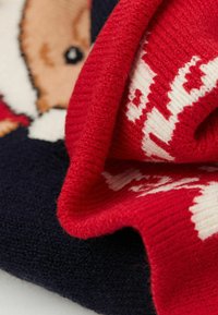 Dzianinowy koc w kolorach czerwonym, granatowym i kremowym. Wzór zawiera postać z kreskówki oraz tekst. Miękka faktura z podwiniętym brzegiem.