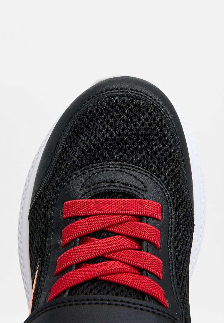 Zapatilla negra con material de malla y sintético, con cordones rojos, puntera redonda y suela de goma blanca.