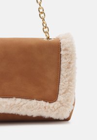 Braune Lederhandtasche mit einem flauschigen cremefarbenen Kunstfellbesatz, abgerundeten Kanten, Kettenriemen und einer weichen Textur.