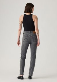 Sivek jeans z visokim pasom, ravnim krojem hlačnic in izrazitimi zadnjimi žepi s prepoznavnim šivom. Obuvene s črno majico brez rokavov.