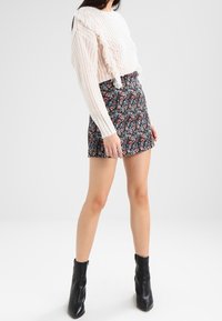 Vit stickad tröja med volangdetaljer, i kombination med en blommönstrad kjol. Svarta ankellånga stövlar fulländar outfiten.