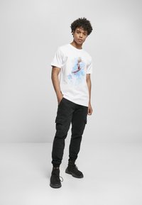 Hvid t-shirt med et farverigt grafisk print af en person, der manipulerer med en basketball, parret med sorte cargo-bukser og sorte sneakers.