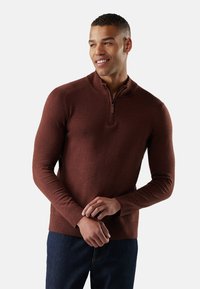 Bordeauxkleurige trui met rits en geribde kraag en manchetten, gemaakt van textuurstof. Gecombineerd met donkere jeans.