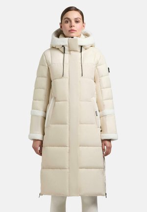 Lange, puffy beige jas met een met bont gevoerde capuchon, doorgestikt ontwerp, zijzakken en zwarte koordjes. Beschikt over witte bontaccenten bij de manchetten.