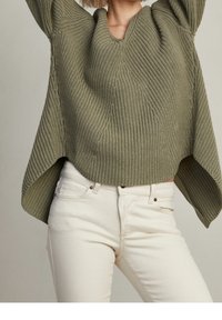 Vihreä neulepaita V-pääntiellä ja leveillä hihoilla, jossa on ribbikuvio. Yhdistetty valkoisiin vartalonmyötäisiin farkkuihin.