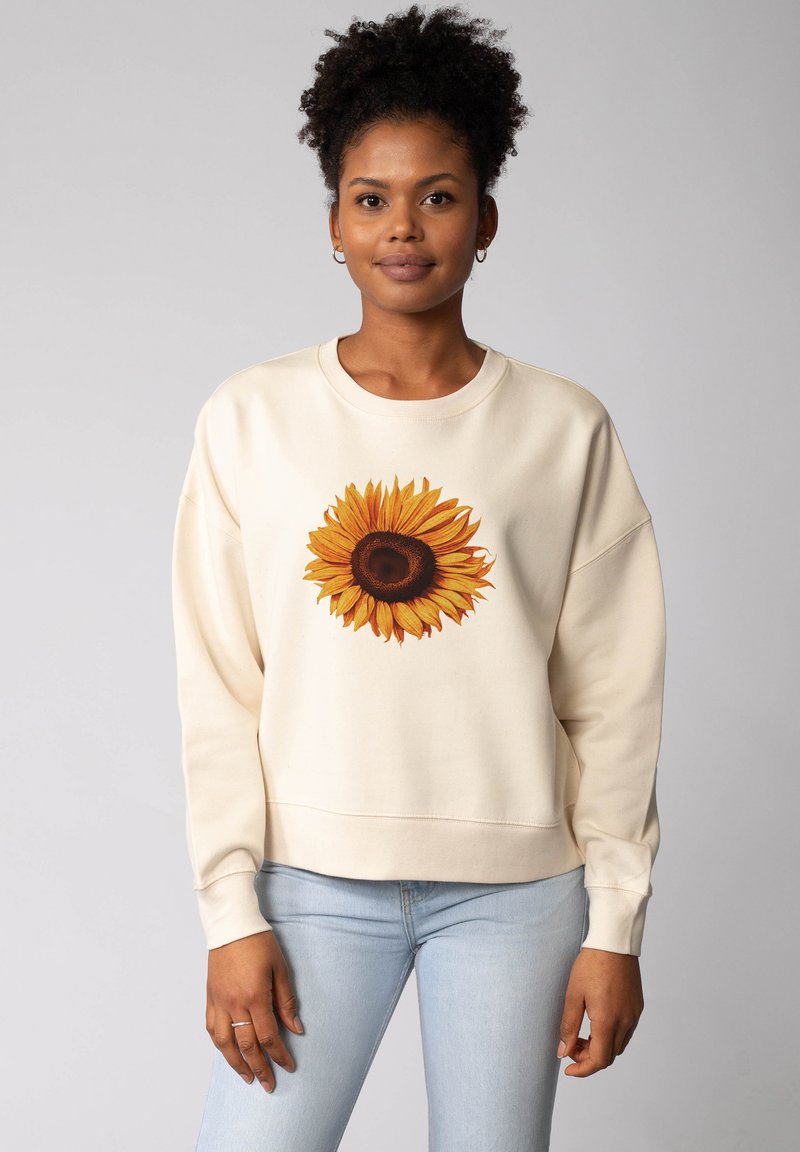 Sweatshirt beige clair avec un grand motif de tournesol en jaune et marron, à la coupe décontractée et avec des poignets et un ourlet côtelés.