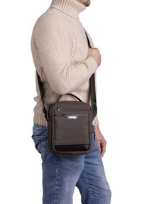 Borsa a spalla grigia con superficie texture, manico superiore e tracolla regolabile, dotata di una tasca frontale e un elegante accento nero.