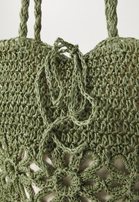 Groene geweven tote bag met een haakpatroon en bloemontwerpen. De handvatten zijn gemaakt van gedraaid materiaal, wat een gestructureerde afwerking laat zien.