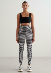 Czarny krótki top zestawiony z legginsami z wysokim stanem, zdobionymi czarno-białym wzorem pepitki. Modelka ma na sobie białe trampki.