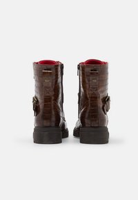 Paire de bottes en cuir marron à motif crocodile avec boucles latérales et doublure intérieure rouge, vues de dos sur fond blanc.