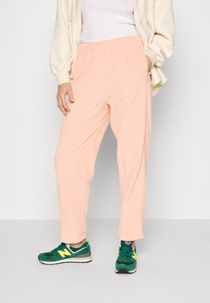 Lichtroze corduroy broek met een elastische tailleband, in een ontspannen pasvorm met omgeslagen hemden, gecombineerd met groene sneakers.