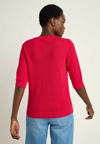 Fitted, short-sleeve sweater in bright pink, textured knit fabric, with a wide neckline and ribbed cuffs and hem. Paired with light blue jeans.