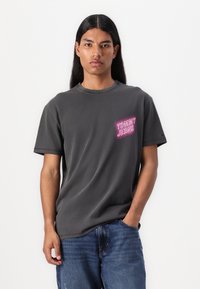 Kulgrå bomulds t-shirt med korte ærmer, rund hals og pink "TOMMY JEANS" logo på venstre brystområde. Casual pasform.