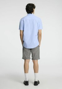 Camicia azzurro chiaro a maniche corte in cotone, abbinata a pantaloni corti grigi arrotolati. Calzini bianchi alla caviglia e scarpe nere completano l'outfit.