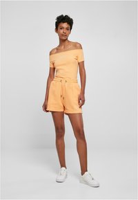Oransje off-shoulder kortermet topp og matchende shorts. Laget av mykt stoff, med snøre i midjen og brodert logo-detalj.