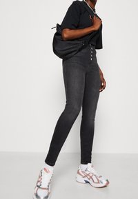 Vaqueros negros de tiro alto y ajuste slim, con cierre de cinco botones, combinados con una camiseta negra y zapatillas deportivas multicolores.