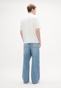 Hvid bomulds t-shirt med rund halsudskæring, parret med lyseblå oversized denim jeans med afslappet pasform og baglommer.