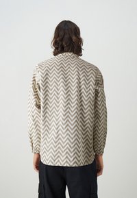 Brown and white chevron-patterned jacket with a relaxed fit, elastic cuffs, and a mandarin collar. Lightweight fabric, visible stitching details.