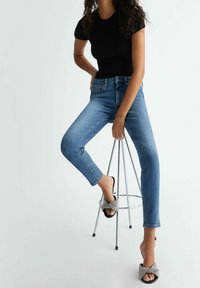 Jeans azules de corte ajustado y lavado claro, combinados con una blusa negra de manga corta con canalé y zapatos negros tipo slip-on con un detalle texturizado.