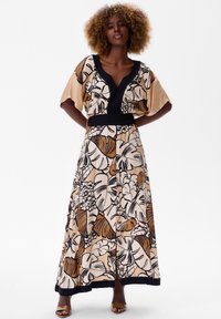 Maxi-jurk in beige en zwart met gedurfde bloemen- en bladerenpatronen. Beschikt over een V-hals en een zwarte tailleband, met vloeiende, korte mouwen.