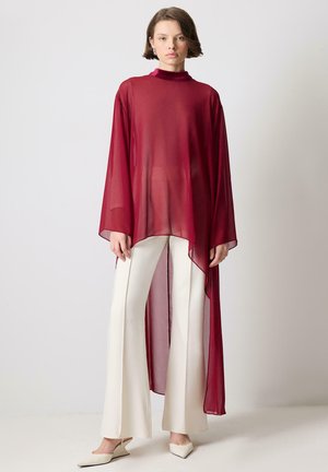 Top lungo trasparente color bordeaux con collo alto, design a strati e spacchi laterali, abbinato a pantaloni a zampa d'elefante di colore crema e ballerine a punta.