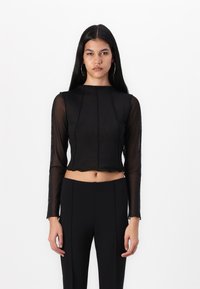 Črni prosojni dolg rokav s visokim ovratnikom in krojenjem, ki se ponaša z diskretnimi šivi. Dopolnjeno s črnimi oprijetimi hlačami.