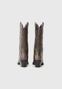Botas de vaquero de piel marrón con detalles bordados, punta afilada y tacones apilados. Presentan tachuelas decorativas y un acabado texturizado.