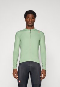 Long-sleeve cycling jersey in light green, featuring a front zipper and slim fit. Paired with black cycling shorts, highlighting athletic design.