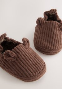 Chaussons en velours côtelé marron avec texture côtelée, bout arrondi et petites oreilles sur les côtés. Intérieur doublé avec un motif à carreaux.