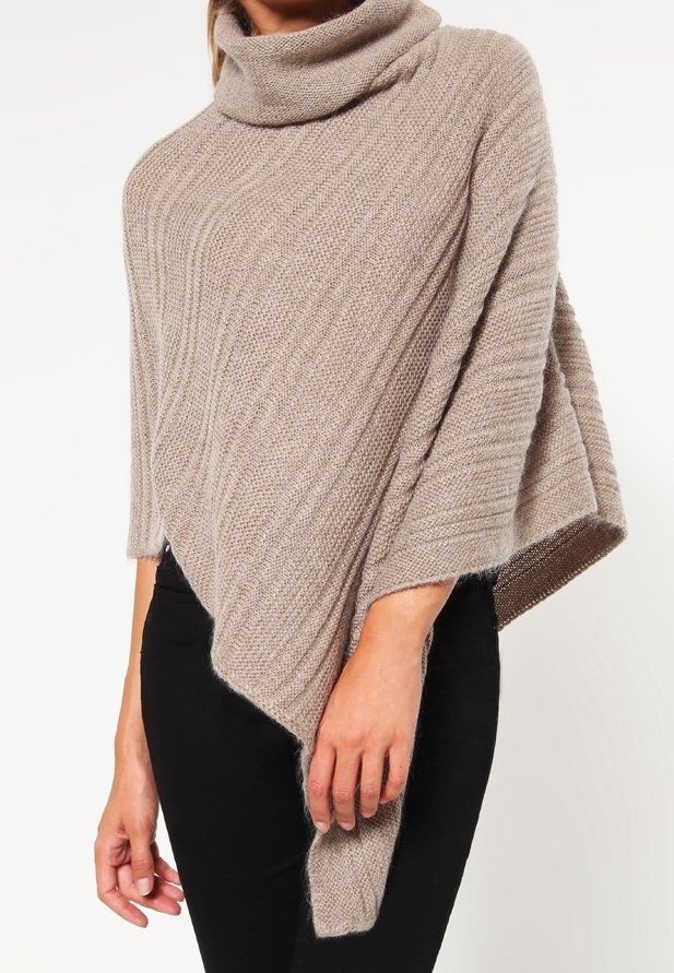 Poncho beige tricoté avec un col haut en forme de cagoule, texture côtelée et ourlet asymétrique. Le matériau semble doux, décontracté et léger.