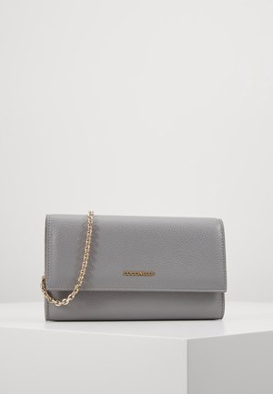 Szary skórzany kopertówka z złotym łańcuszkowym paskiem i małym złotym logo „Coccinelle” umieszczonym na środku przedniej klapy, ustawiona na białym piedestale.